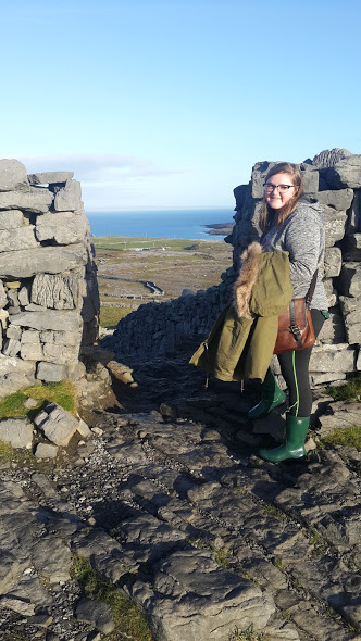 Bri standing at the entrance of fort Angus on the Island of Inishmore. The rolling green landscape in the background.