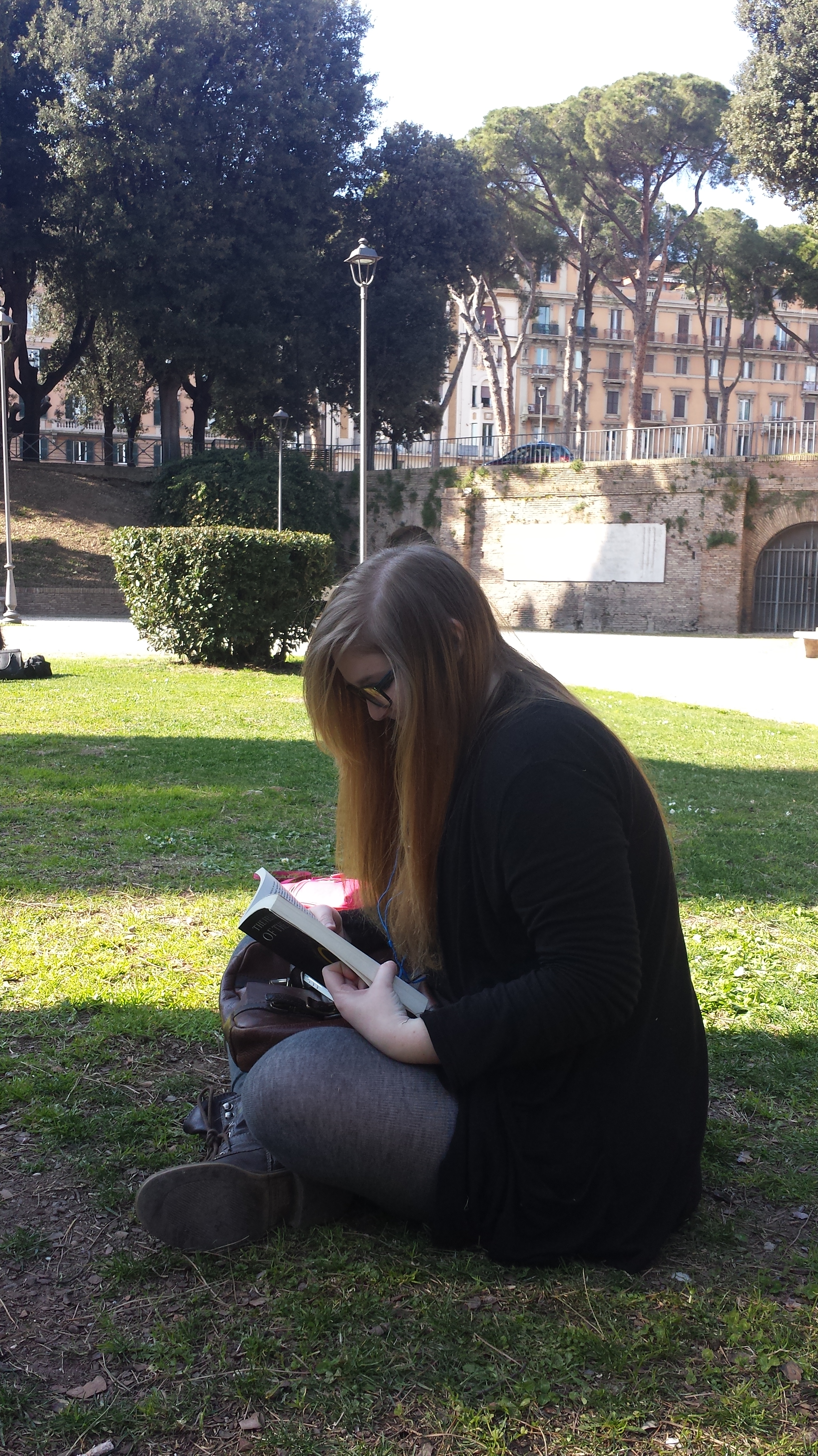 A Picture of Bri sitting in the Park behind the Castel Sant'Angelo. She is looking down at the book, with her legs crossed infront of her.
