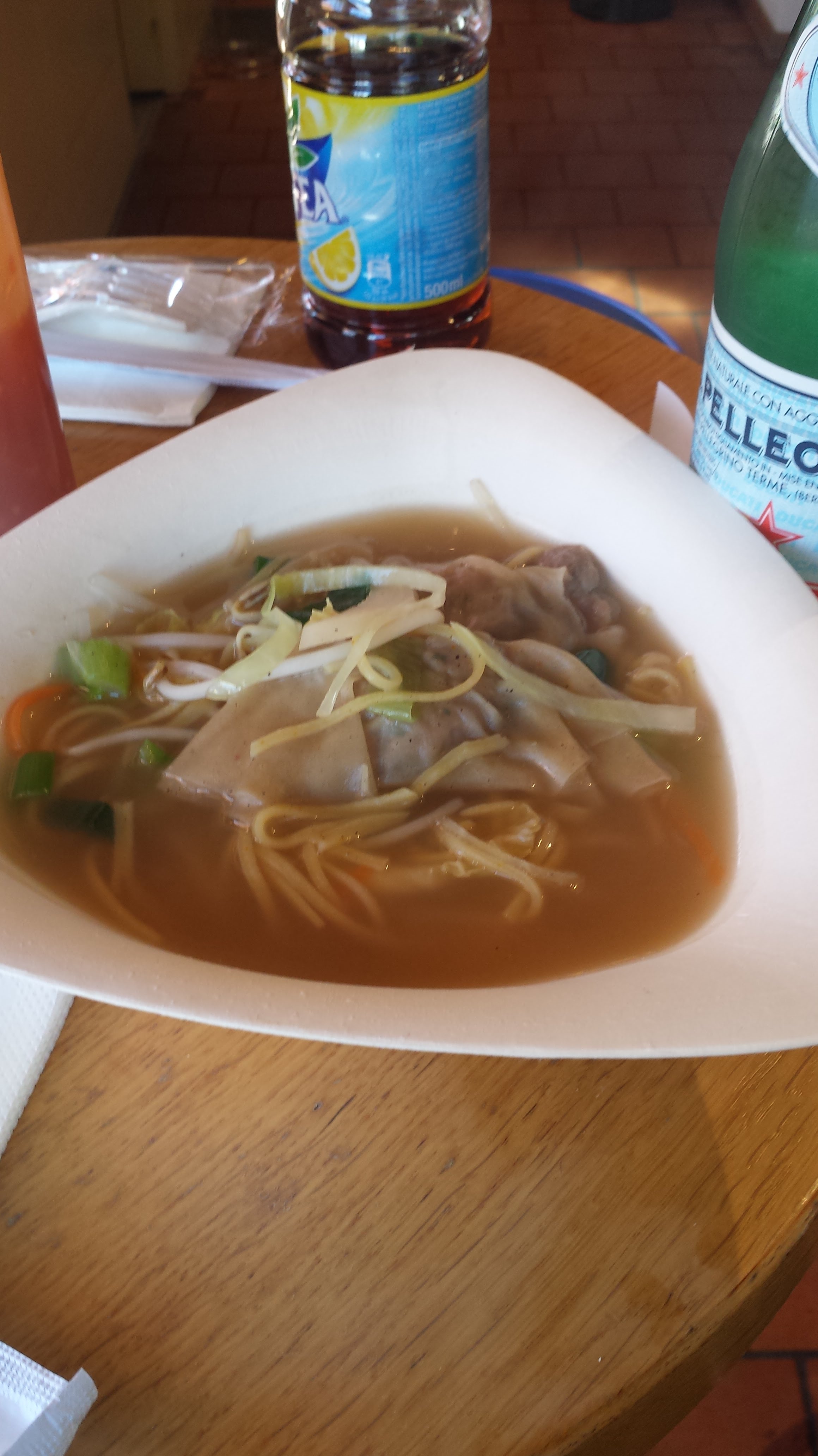 A picture of a bowl of wonton soup, with soft drinks in the background.