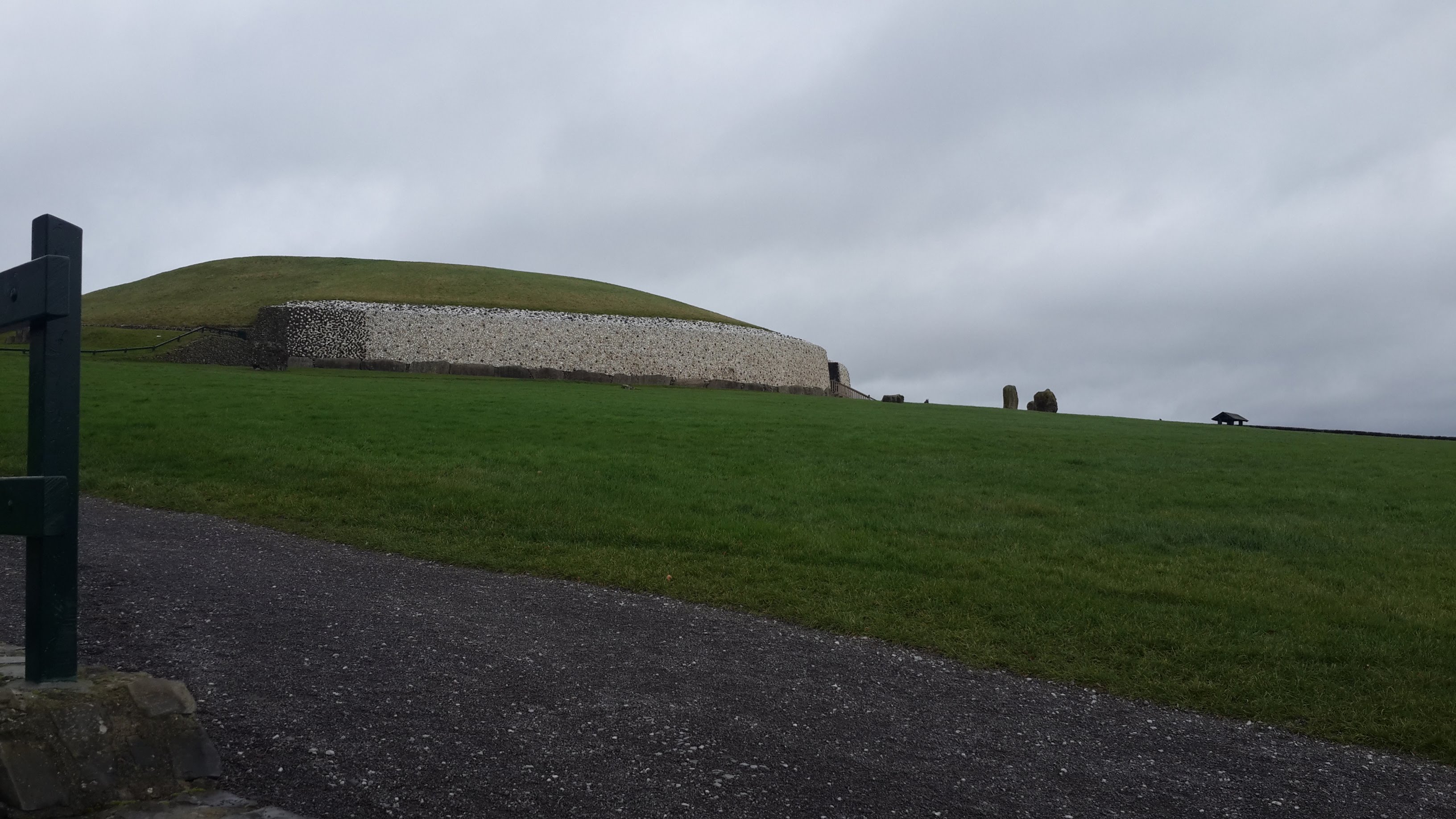 The Tomb of newgrange viewed from the bottom of the hill it was built on. It is a cloudy day, and the grass is particularly green against the contrast of the white stone of Newgrange.