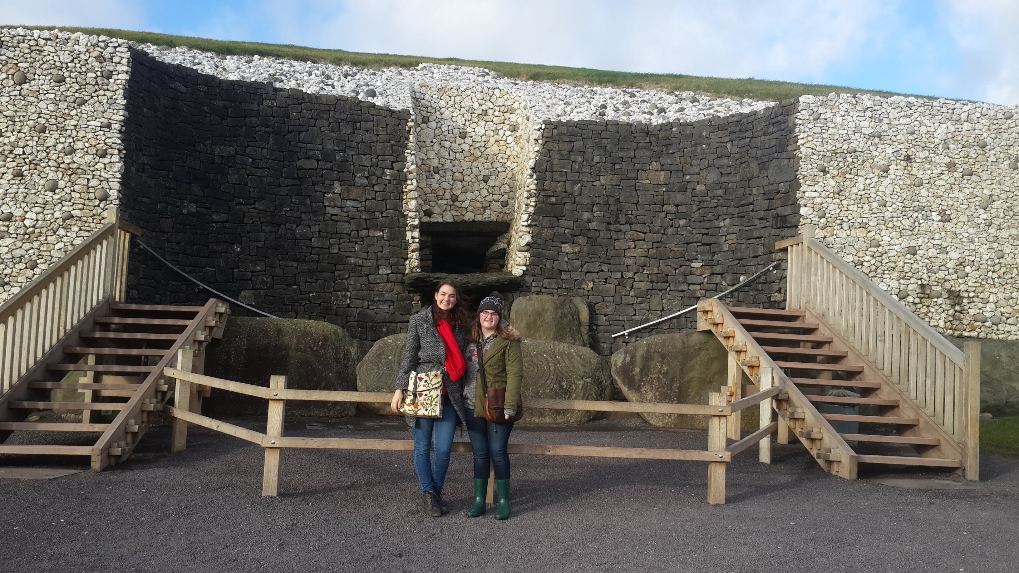 Bri and her friend Catherine standing infront of the white and grey stone entrance of Newgrange. The carved standing stone sits behind them.