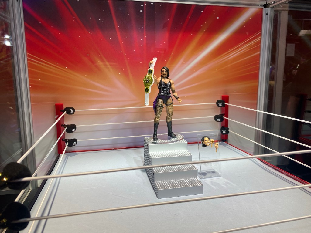 A picture of WWE star Rhea Ripley action figure posing in a ring with the Women's belt. 