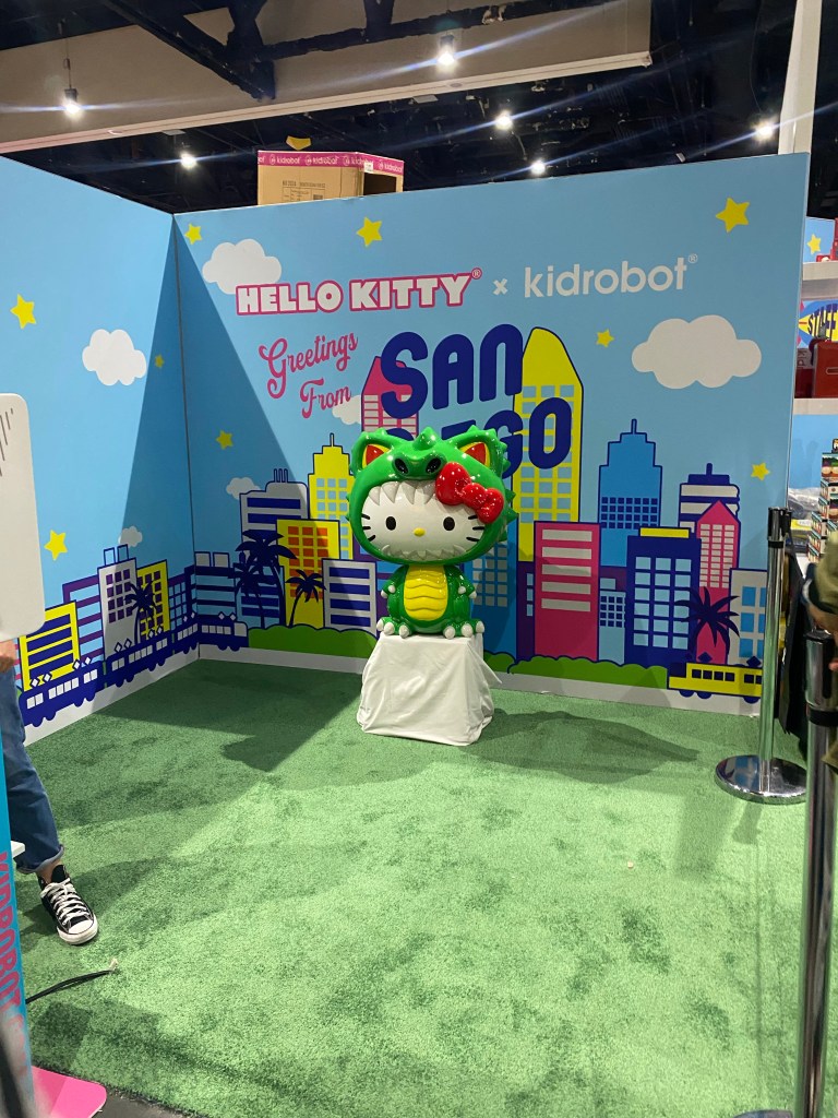A picture of a Hello Kitty statue dressed in a dragon costume that people are waiting in line to take pictures with.